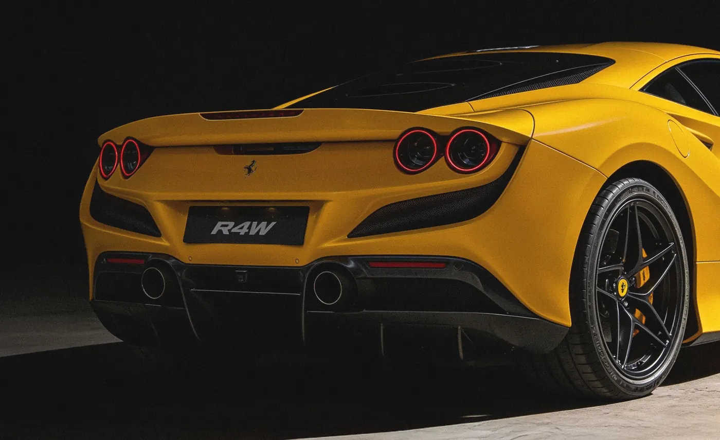 A yellow Ferrari F8 Tributo with a RAW badge, lit against black