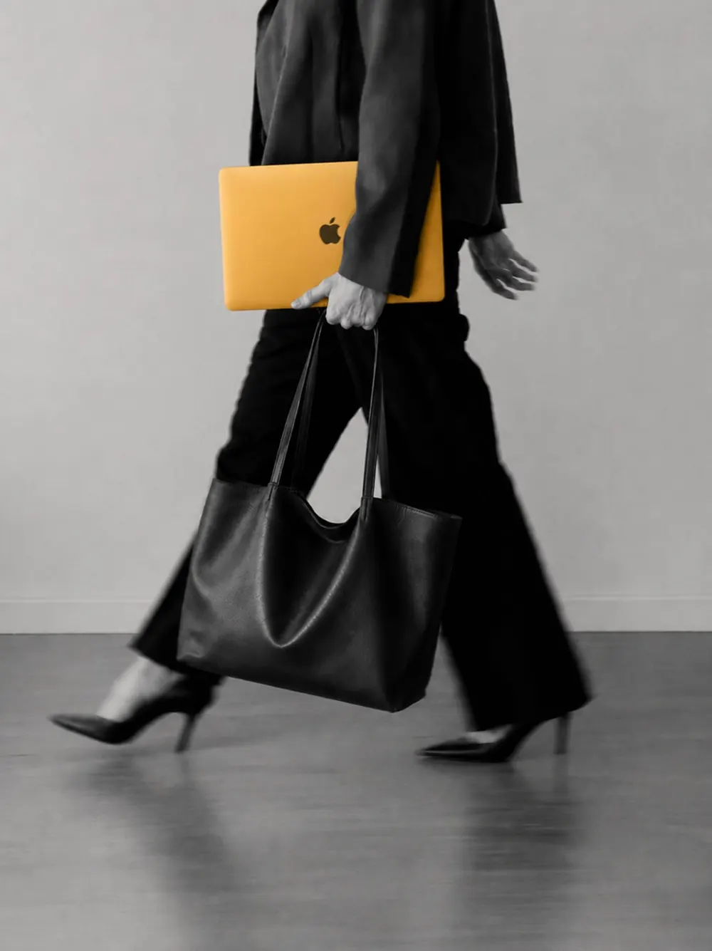 A woman in black walking with a laptop and leather tote